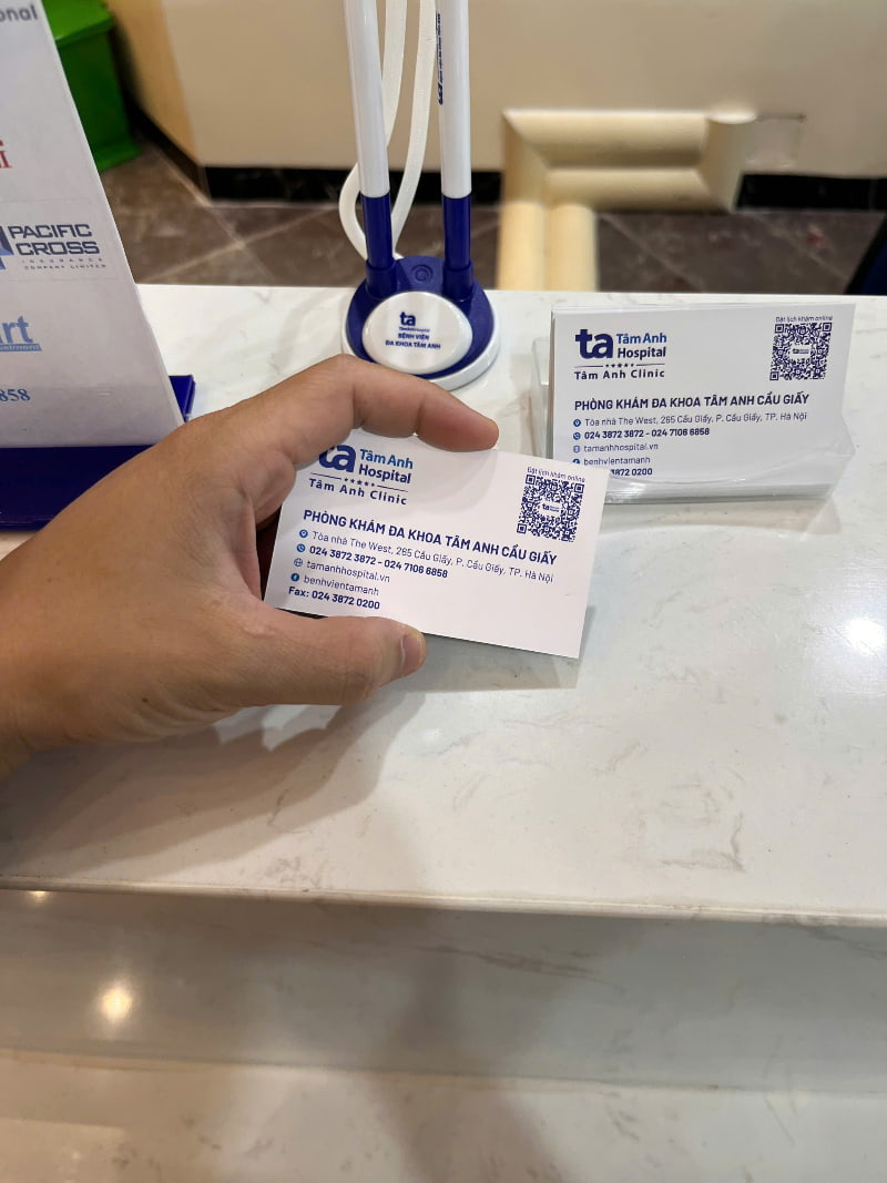 Cận cảnh tay cầm danh thiếp Phòng khám Đa khoa Tâm Anh Cầu Giấy tại quầy lễ tân