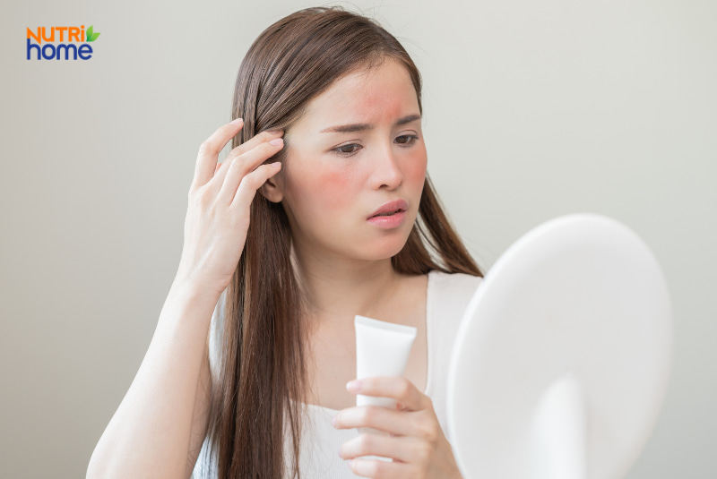 Cô gái lo lắng nhìn vào gương với vùng má bị đỏ, dấu hiệu kích ứng da
