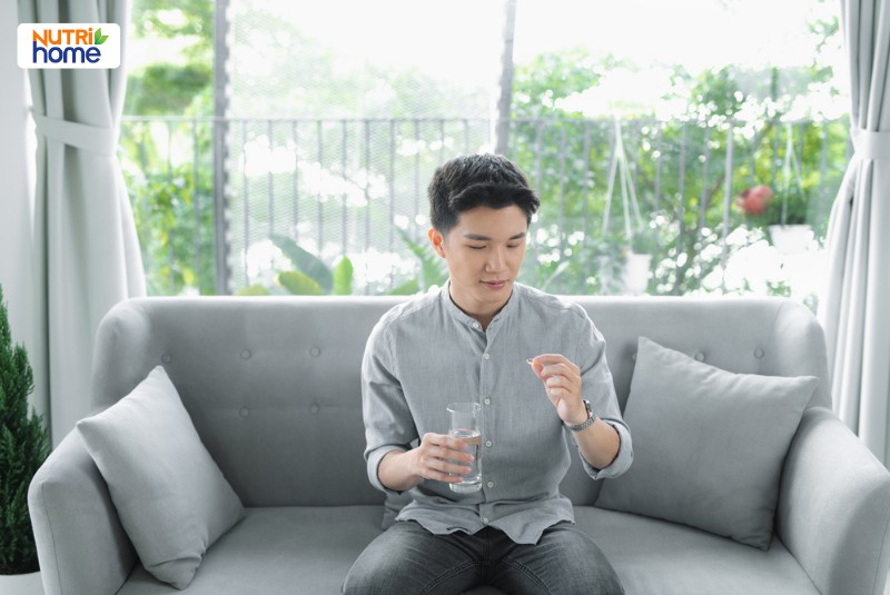 Nam giới ngồi trên ghế chuẩn bị uống thuốc hoặc bổ sung sau tiêm phòng