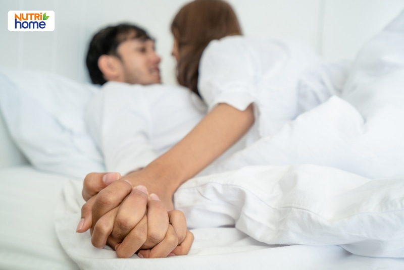 Cặp đôi nằm gần gũi và nắm tay nhau trên giường.
