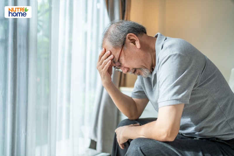 Người cao tuổi ngồi mệt mỏi và ôm trán tại nhà.