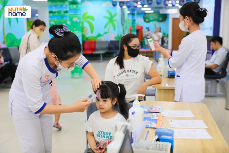 Nhân viên y tế đo thân nhiệt cho trẻ trước khi tiêm.