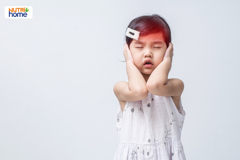 Bé gái nhắm mắt, ôm hai bên đầu với biểu hiện khó chịu.