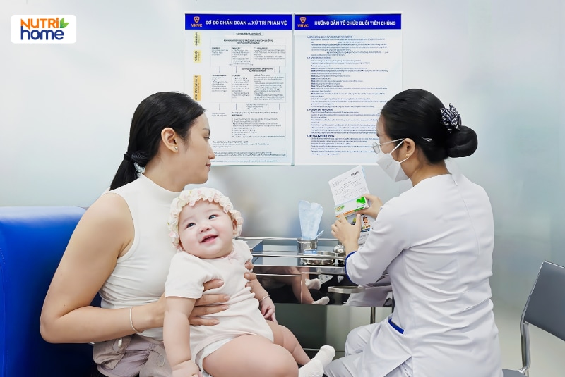 Nhân viên y tế giới thiệu hộp vắc xin cho người mẹ đang bế bé gái