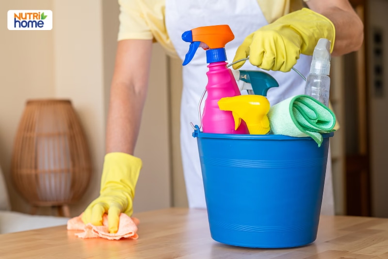 Người đeo găng tay vàng lau bàn cùng xô đựng chai xịt và khăn lau.