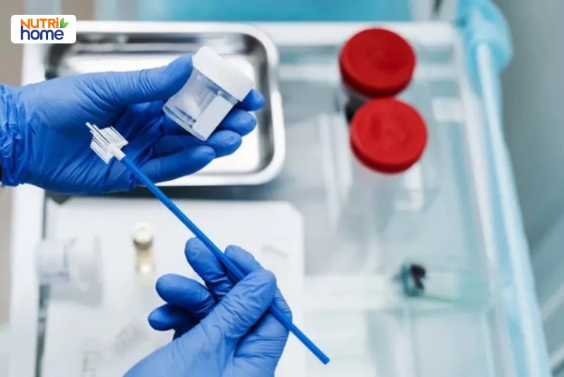 Nhân viên y tế cầm que lấy mẫu và ống đựng bệnh phẩm xét nghiệm HPV.