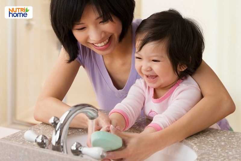 Người mẹ hướng dẫn bé gái rửa tay bằng xà phòng dưới vòi nước