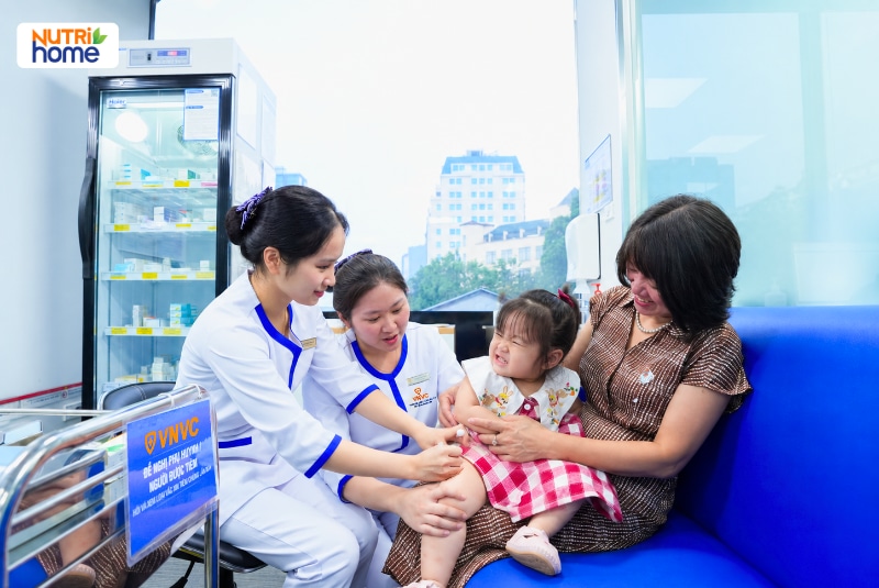 Nhân viên y tế tiêm vắc xin cho bé gái ngồi cùng người thân