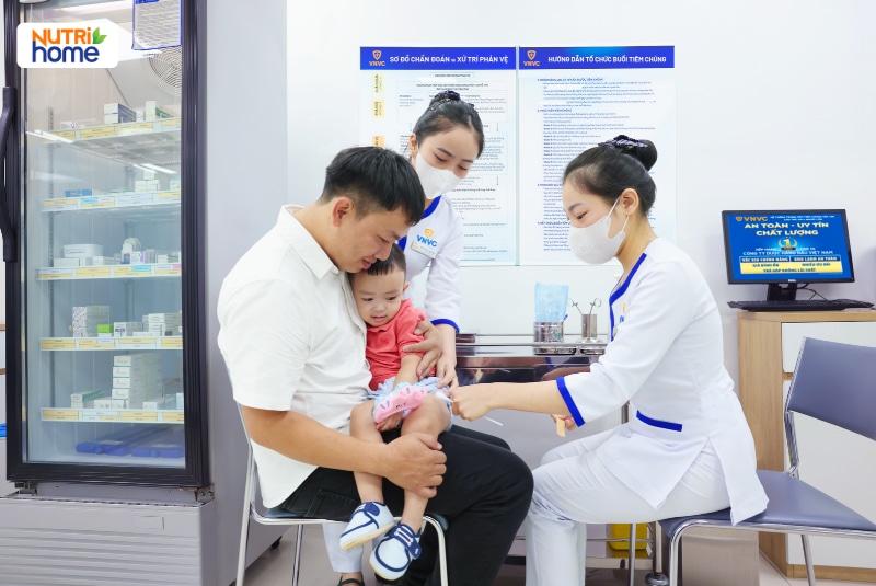 Bé trai được bố bế khi điều dưỡng tiêm vắc xin tại trung tâm