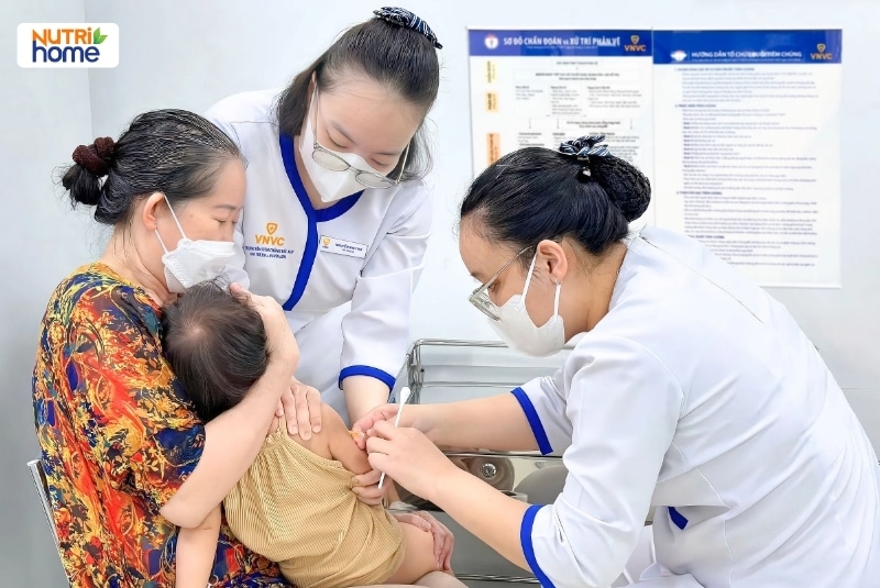 Nhân viên y tế VNVC tiêm vắc xin cho trẻ nhỏ đang được mẹ ôm trong phòng tiêm