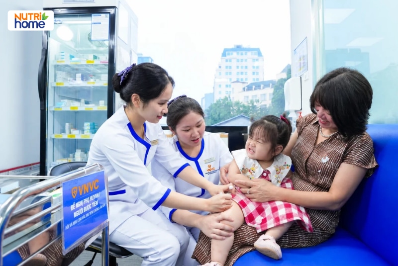 Hai điều dưỡng VNVC tiêm vắc xin cho bé gái ngồi cùng người thân